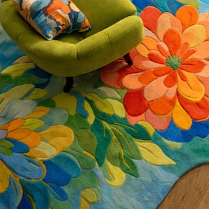 May include: A vibrant, floral-patterned rug with a large orange and red flower design. The rug features blue, green, and yellow leaves and petals. A green armchair and patterned pillow are in the upper left corner.