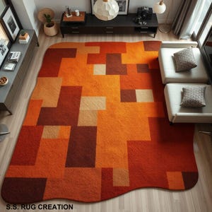 May include: A large, rectangular rug with a geometric pattern in shades of orange, brown, and beige. The rug's design features a series of interconnected blocks, creating a modern and abstract aesthetic. The rug is placed on a wooden floor.