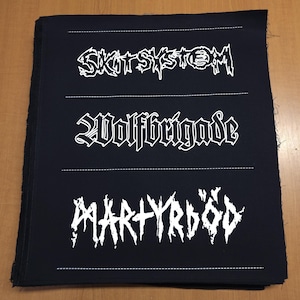 Könnte beinhalten: Schwarze Stoffaufnäher mit weißem Text. Der obere Aufnäher lautet "SKITSYSTEM", der mittlere Aufnäher lautet "WOLFBRIGADE" und der untere Aufnäher lautet "MARTYRDÖD". Jede Textzeile ist durch eine gestrichelte weiße Linie getrennt.