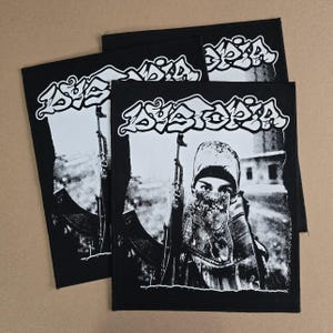 May include: Black and white patches featuring the word "Dystopia" in a stylized font. The patches depict a person holding a rifle, with a blurred background. The patches are rectangular and have a black border.