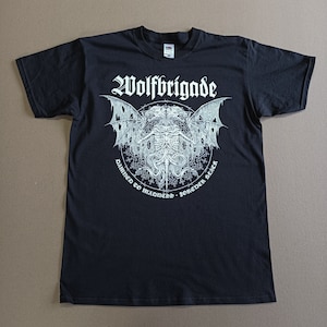 May include: Black t-shirt with a white graphic print of a winged skeletal creature with the text "Wolfbrigade" above it and "Damned to Madness - Forever Black" below it.