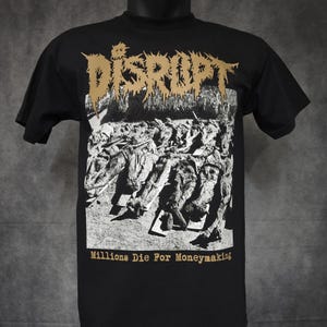Peut inclure: T-shirt noir avec le mot "DISRUPT" en or vieilli au-dessus d'une image en niveaux de gris de corps. Le texte "Millions Die For Moneymaking" est en dessous. Le t-shirt est présenté sur un mannequin.