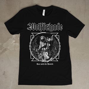 Puede incluir: Camiseta negra con un gráfico blanco. El texto "Wolfbrigade" está sobre una ilustración de una figura esquelética con alas y una guadaña, dentro de un borde de cadena. El texto "Run with the Hunted" está debajo.