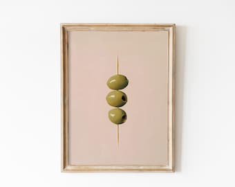 May include: A framed print of a minimalist still life featuring three green olives skewered on a toothpick against a pale pink background.
