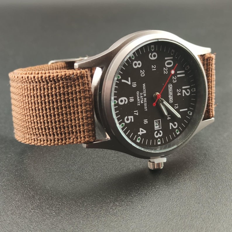 May include: A wristwatch with a brown canvas band and a black face. The watch has white numerals and hands, with a red second hand. The watch face includes the text "WATER RESIST 3 ATM QUARTZ".