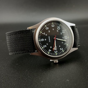 May include: A black analog watch with a silver-colored case and a black nylon strap. The watch face is black with white numerals and hands, and a red second hand. The watch is a quartz movement.