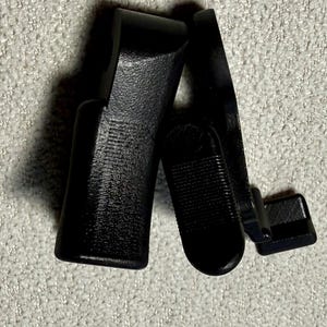 May include: Black plastic car part, possibly a window or door component. The pieces have a textured surface and are arranged at an angle against a light gray background. The parts appear to be new.