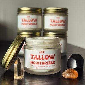 May include: A glass jar of Sol Organics Tallow Moisturizer with a gold lid. The jar is open and the cream is visible. The label on the jar says "Tallow Moisturizer" and "SPF 8 | Made with Grass Fed Beef Tallow | 2 oz | @soulskinorganics".