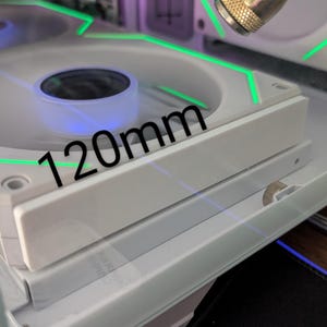 Könnte beinhalten: Nahaufnahme eines weißen Computerlüfters mit einem Durchmesser von 120 mm, beleuchtet mit grünen und blauen Lichtern. Der Lüfter ist Teil eines Computergehäuses, mit sichtbaren Komponenten.