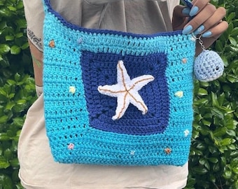 May include: A blue and white crocheted bag with a starfish design. The bag has a strap and a small blue crocheted charm attached to it.
