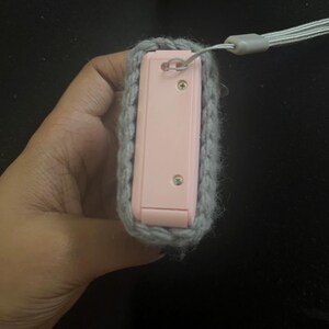 May include: A pink camera case with a grey crocheted cover and a grey strap.