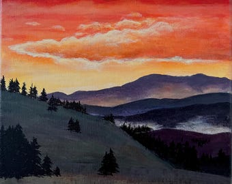 May include: An original landscape painting depicts a mountain range under a vibrant sunset. The sky transitions from fiery red to golden yellow, with fluffy clouds. Dark green hills are dotted with trees, creating a serene, natural scene.