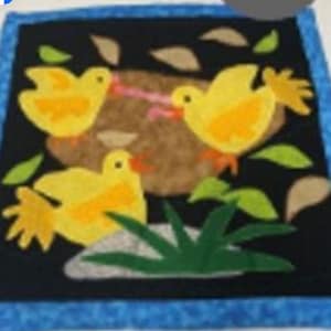 May include: A square, quilted wall hanging featuring three yellow birds with orange feet and beaks, set against a black background. The birds are surrounded by green leaves and brown patches, with a blue border.