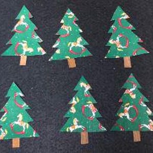 May include: Six flat, triangular Christmas tree cutouts made of green paper with a repeating pattern of white and tan rocking horses. Each tree features a small, rectangular brown paper trunk at the base, arranged in two rows of three.