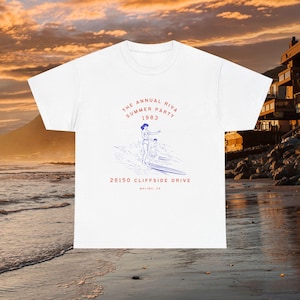 May include: White t-shirt with a blue and red graphic of a woman and man surfing. The graphic includes the text "The Annual Riva Summer Party 1983" and "28150 Cliffside Drive Malibu, CA".