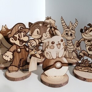 Peut inclure: Un ensemble de sept figurines en bois de personnages de jeux vidéo populaires, dont Mario, Sonic, Pikachu, Crash Bandicoot et un dragon. Les figurines sont posées sur de petites bases en bois.