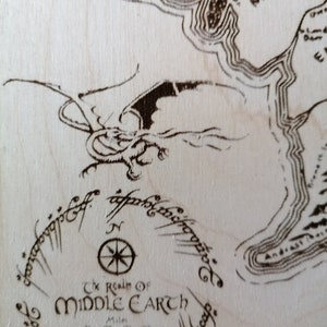 May include: A close-up of a wooden map of Middle-earth, featuring a compass and the inscription "The Realm of Middle-earth".