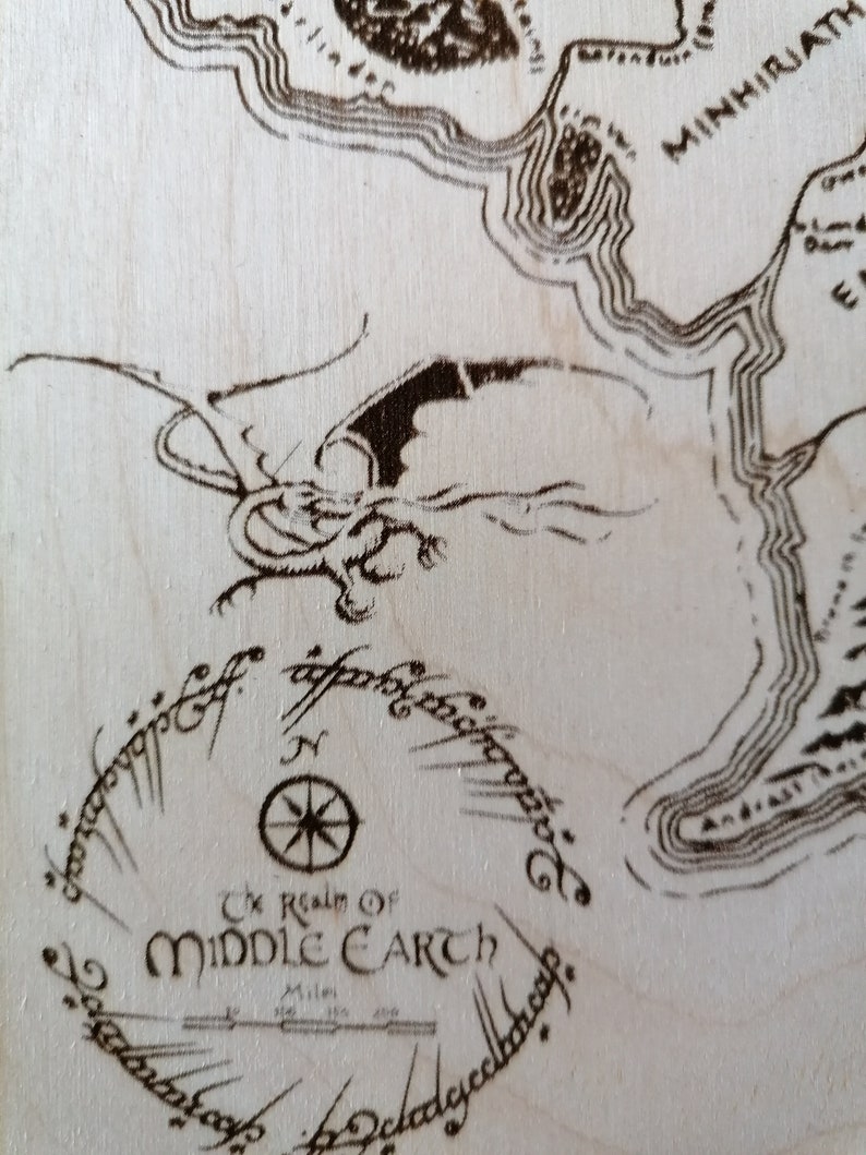 May include: A close-up of a wooden map of Middle-earth, featuring a compass and the inscription "The Realm of Middle-earth".