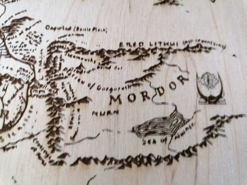 May include: A close-up of a wooden map of Middle-earth, showing the land of Mordor. The map is burned into the wood, with the text "Mordor" clearly visible. The text "Sea of Nurn" is also visible.