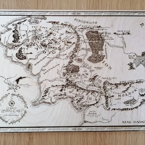 May include: A wood-burned map of Middle-earth from The Lord of the Rings. The map shows the major regions of Middle-earth, including Mordor, Rohan, and Gondor. The map is surrounded by a decorative border.