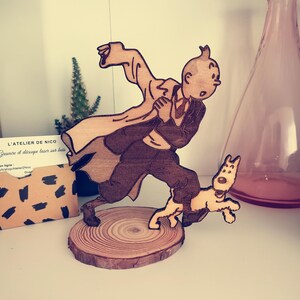 Könnte beinhalten: Eine Holzfigur von Tim, einer fiktiven Figur aus der belgischen Comicserie Die Abenteuer von Tim, die mit seinem Hund Struppi rennt. Die Figur steht auf einem Holzsockel.