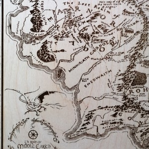 May include: A wood-burned map of Middle-earth from The Lord of the Rings. The map shows the land of Mordor, the Shire, and the surrounding areas. The map is surrounded by a circle with the text "The Realm of Middle-earth" and a scale in miles.