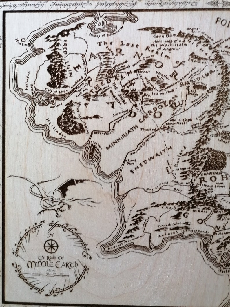 May include: A wood-burned map of Middle-earth from The Lord of the Rings. The map shows the land of Mordor, the Shire, and the surrounding areas. The map is surrounded by a circle with the text "The Realm of Middle-earth" and a scale in miles.