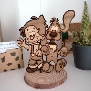 Op de afbeelding: Een houten figuur van een jongen en zijn hond. De jongen draagt een overall en de hond heeft slappe oren. De figuur staat op een houten voet.