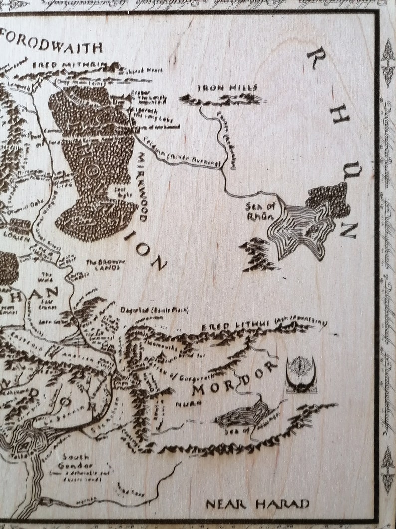 May include: A detailed map of Middle-earth from J.R.R. Tolkien's The Lord of the Rings, featuring the land of Mordor, the Iron Hills, and the Sea of Rh&ucirc;n. The map is printed on a light brown wooden surface.