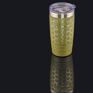 May include: A green stainless steel tumbler with a honeycomb pattern and the name "James" engraved on it. The tumbler has a lid and is sitting on a black surface.