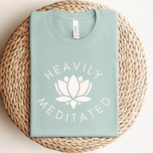 May include: A light blue t-shirt with a white lotus flower and the text "Heavily Meditated" printed on the front.