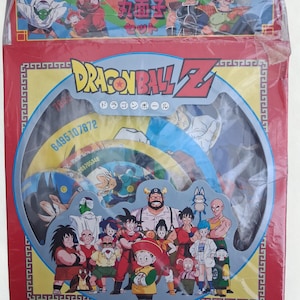 May include: A red Dragon Ball Z boxed set featuring various characters from the anime series. The box has a circular window displaying colorful discs with character illustrations. The top of the box has Japanese text and character art.