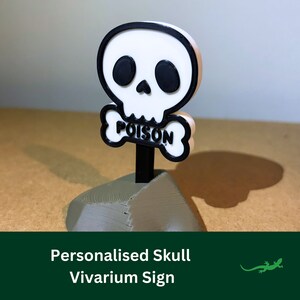 May include: A 3D printed skull and crossbones sign with the word "POISON" on the crossbones. The sign is white with black accents and is mounted on a grey base.
