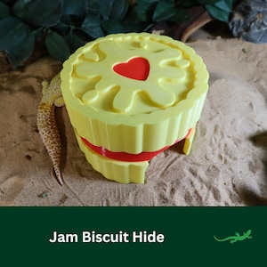 May include: A yellow and red plastic hide shaped like a jam biscuit, with a heart-shaped design on the top. The hide is designed for small reptiles and amphibians.