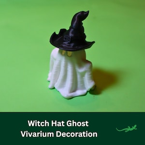 May include: A white ghost figurine wearing a black witch hat. The ghost is sitting on a green surface. This is a Halloween decoration for a terrarium or vivarium.