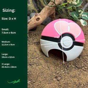 May include: A pink and white Pokeball-shaped reptile hide with a diameter of 15 cm and a height of 12 cm. The hide is made of plastic and has a smooth surface. It is designed to provide a safe and comfortable hiding place for reptiles.