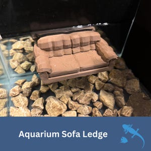 May include: A brown aquarium sofa ledge, designed to provide a decorative resting spot for aquatic pets. The ledge is placed in an aquarium with small rocks. The text "Aquarium Sofa Ledge" is displayed at the bottom of the image.
