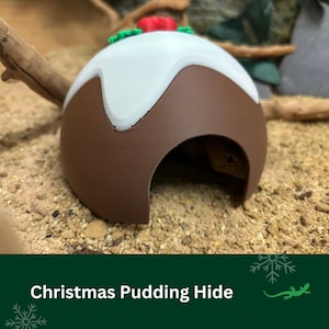 May include: A brown and white ceramic Christmas pudding hide for small reptiles. The hide has a white icing design and a red candy on top.