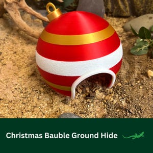 May include: A red and white Christmas bauble with gold stripes, designed as a ground hide for small reptiles. The bauble has a large opening for easy access.