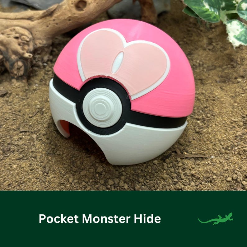 May include: A pink and white Poke Ball with a heart-shaped design on the top. The Poke Ball is made of plastic and has a small opening on the side.