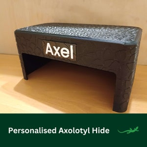 May include: Black plastic hide for an axolotl with a personalised name tag that says "Axel".