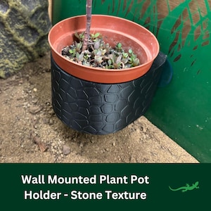 May include: A black wall-mounted plant pot holder with a stone texture. The holder is designed to hold a small plant pot. The pot holder is mounted to a wall with a screw.