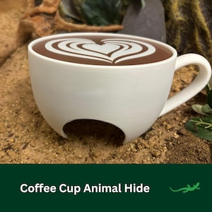 Könnte beinhalten: Eine weiße Keramik-Kaffeetasse mit einem braunen Herzdesign auf der Oberfläche. Die Tasse hat ein Loch im Boden, wodurch sie sich als Versteck für Tiere eignet.