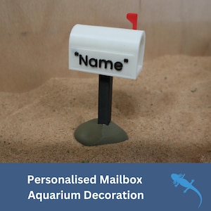 May include: White mailbox aquarium decoration with a black post and a gray base. The mailbox has a red flag and the text "Name" on the front.