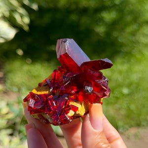 Puede incluir: Un racimo de estructuras cristalinas translúcidas de color rojo intenso que crecen sobre una base mineral texturizada de color amarillo mostaza. Las formaciones cristalinas afiladas y puntiagudas muestran una superficie brillante y reflectante.