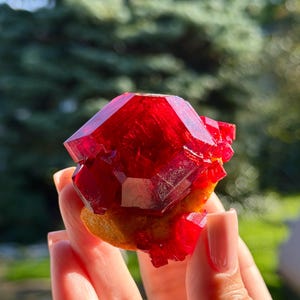 Puede incluir: Un espécimen mineral cristalino de color rojo intenso y vibrante con facetas geométricas afiladas y una textura translúcida similar al vidrio. El grupo muestra un rico tono carmesí con una base sólida y texturizada.