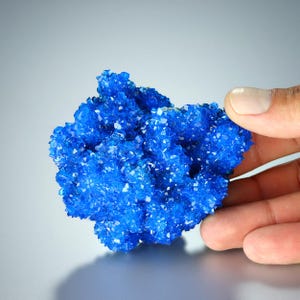 May include: A cluster of vibrant blue crystals, resembling a small mountain range, with a sharp, faceted texture. The crystals are densely packed together, creating a visually striking and intricate formation.