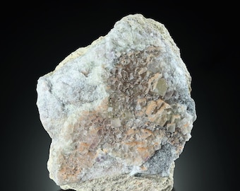 May include: A rough, gray rock with embedded crystals of clear, white, and pink fluorite. The fluorite crystals are clustered together in a random pattern.