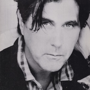 Könnte beinhalten: Schwarz-Weiß-Porträt eines Mannes mit dunklem Haar und ernstem Gesichtsausdruck. Er trägt ein kariertes Hemd unter einer dunklen Jacke. Der Text "New LPs" ist oben links sichtbar.