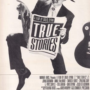 May include: A black and white film poster for True Stories, showing a figure wearing a cowboy hat, sunglasses, and a suit, holding a newspaper with the title True Stories. The text reads It's a completely cool, multi-purpose movie and lists credits.